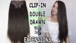 Ekstenzije za kosu Clip-in Double Drawn 50cm 160g, prikazane na slici s tamnom kosom i modelom koji nosi bijelu majicu.
