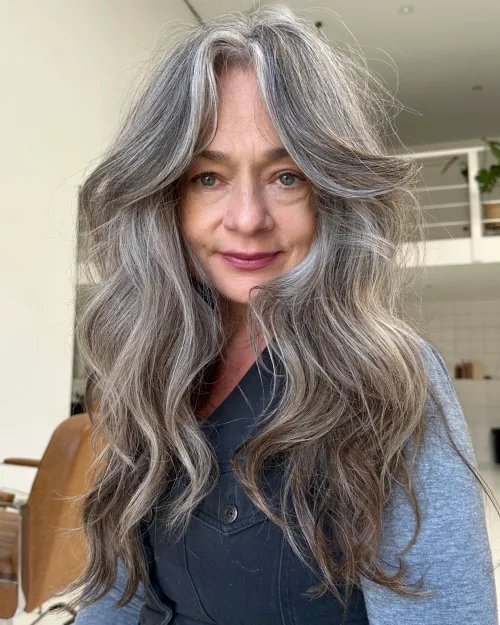 Dugi greige shag sa zavjesa šiškama koje uokviruju lice i stvaraju mekan, ženstven, pomlađujući efekt.