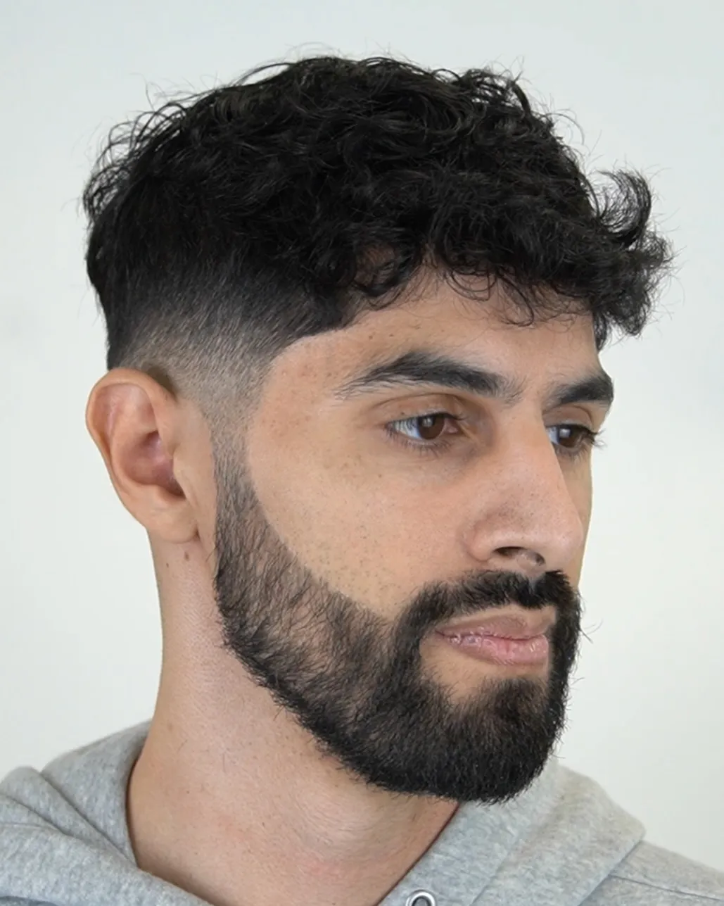 Kovrčava muška frizura s low fade prijelazom koja omekšava snažnu čeljust i naglašava crte kvadratnog lica.