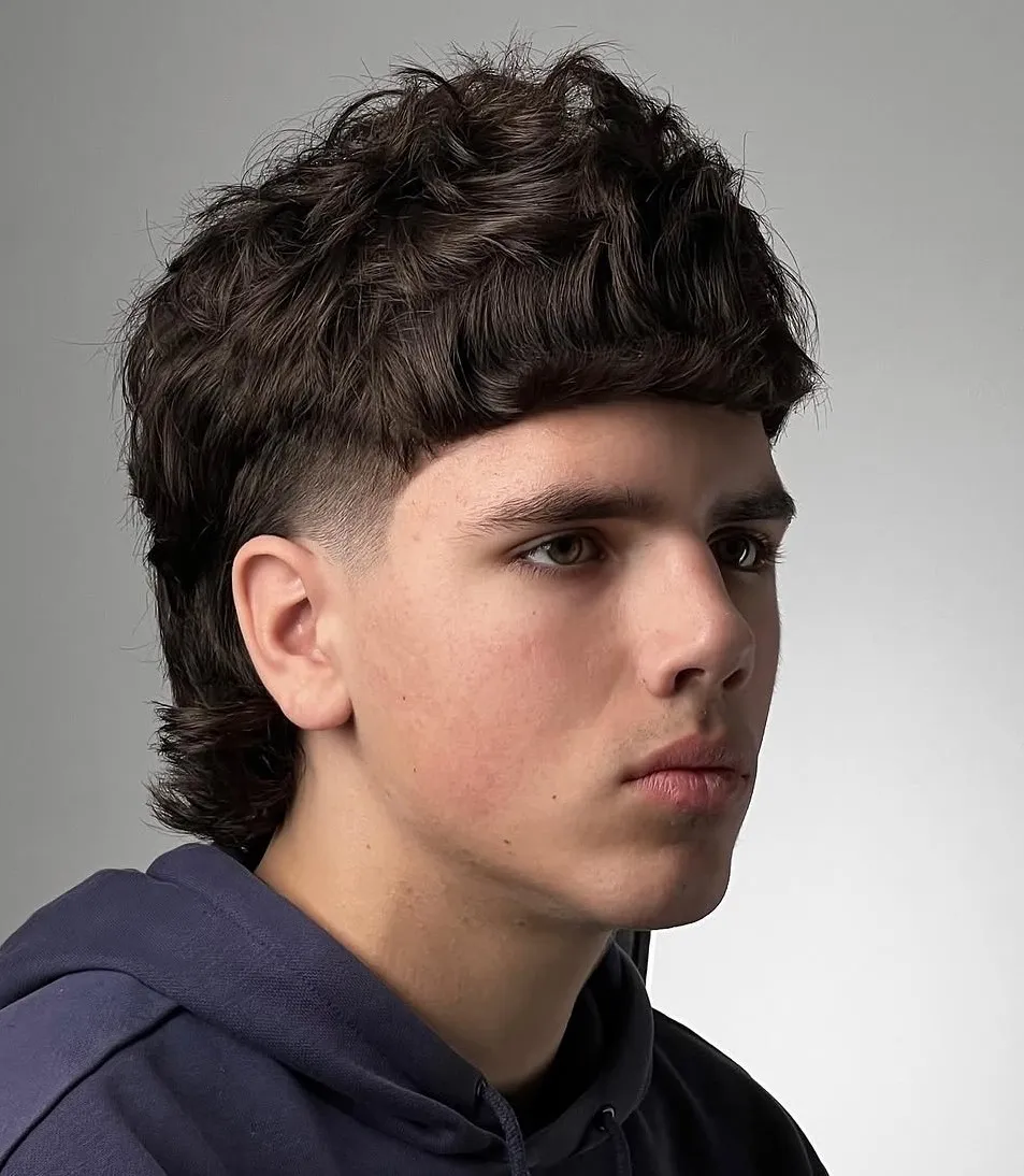 Messy mullet muška frizura s kovrčama koja dodaje volumen i naglašava prirodne linije ovalnog lica.