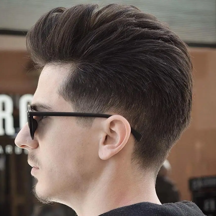 Pompadour frizura s fade prijelazom koja oblikuje gustu kosu u uredan, moderan stil.