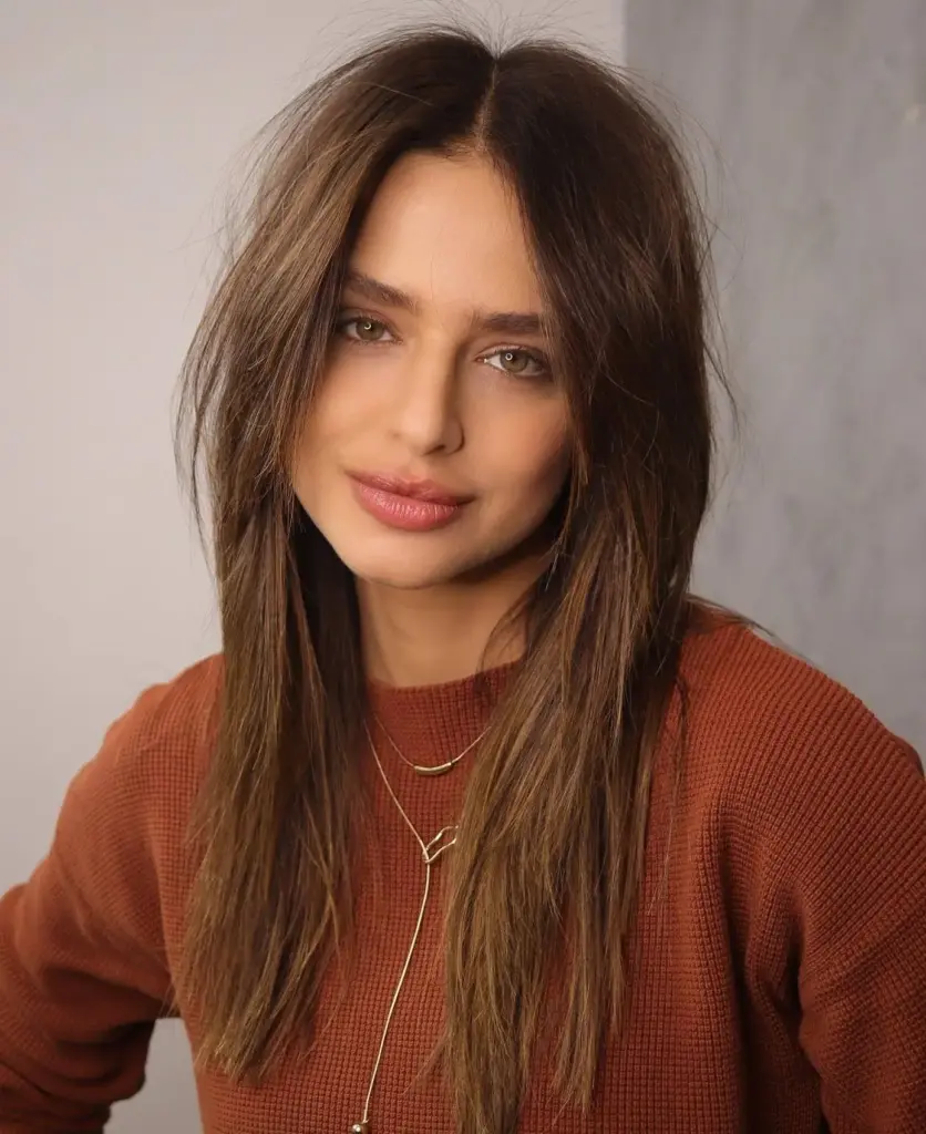 Duga ravna kosa s lagano razbarušenim vrhovima i pramenovima koji uokviruju lice. Frizura izgleda prirodno, mekano i elegantno, s naglaskom na pokret i profinjene linije.