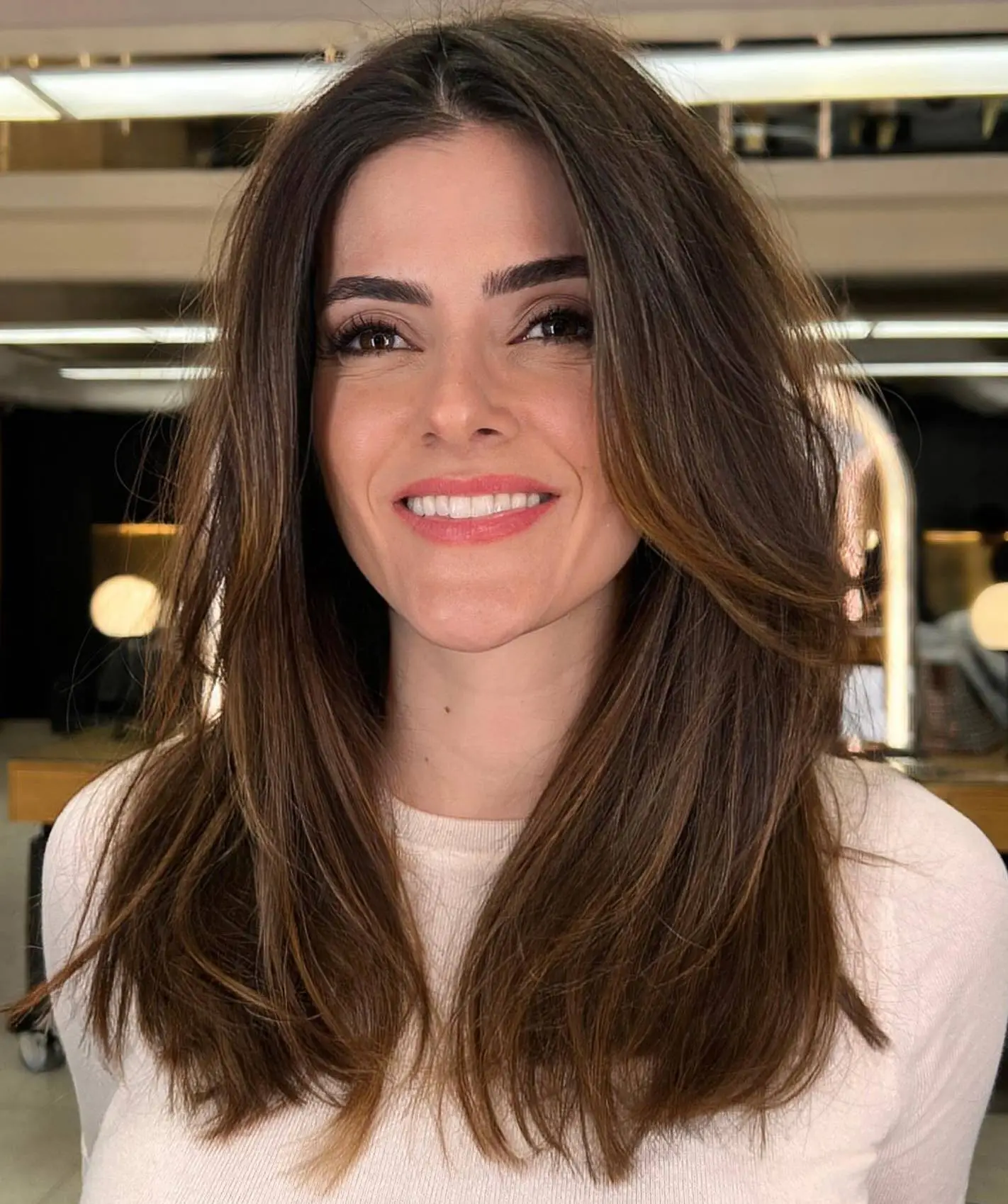 Srednje duga frizura sa slojevima po dužini koja omekšava crte i uravnotežuje trokutasto lice.