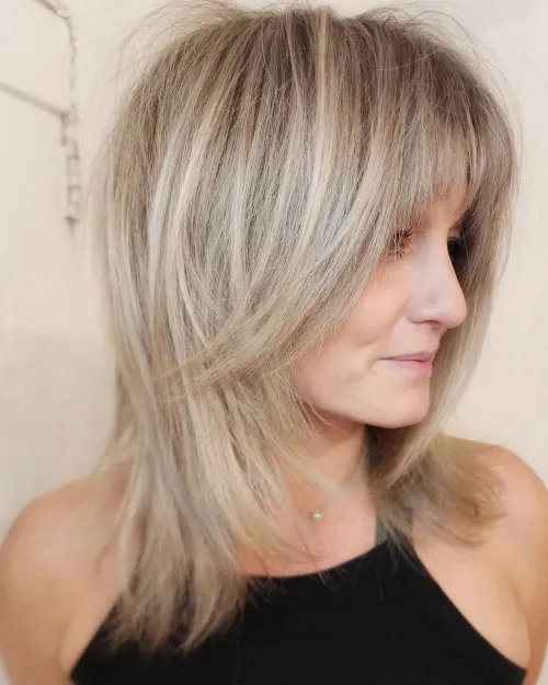 Svijetla ravna shag frizura s nježnim pramenovima koji osvjetljavaju lice i ističu prirodan sjaj kože.