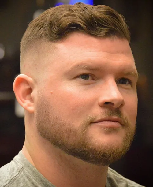 Valovita fade frizura za muškarce s okruglim licem koja dodaje volumen na vrhu i stvara izdužen izgled.