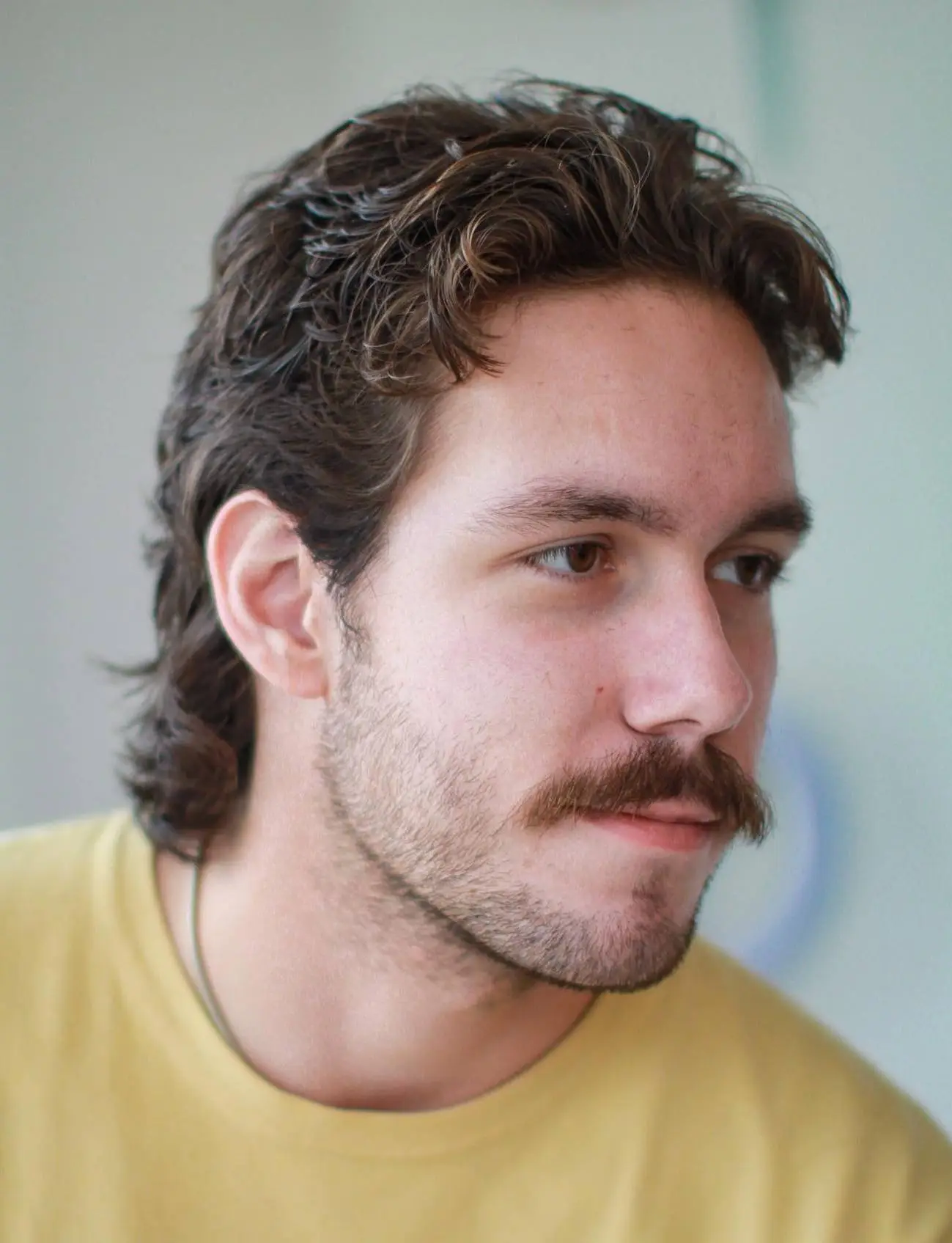 Valoviti mullet frizura koja prirodno prekriva visoko čelo i uravnotežuje proporcije lica.